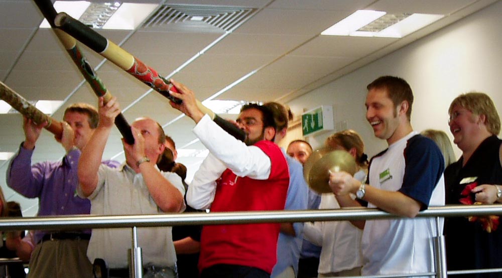 colleagues laughing as three men play didgeridoo in a world music energiser