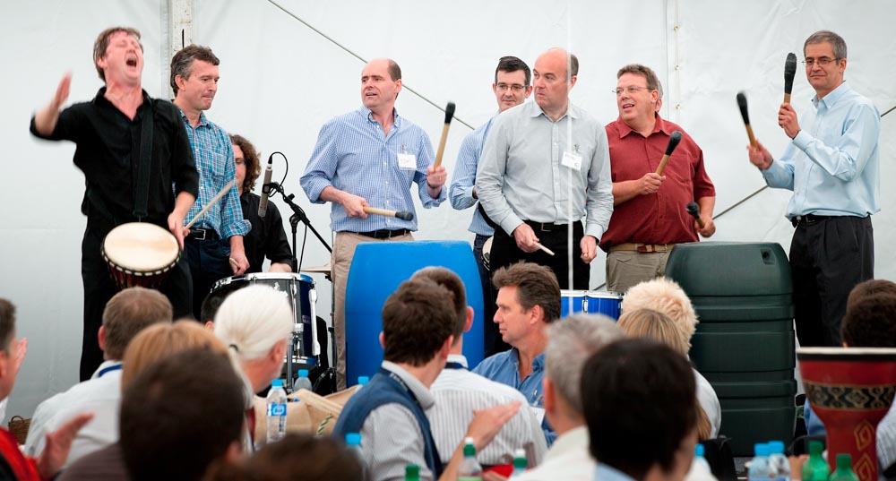 Mark Walker leading a samba energiser with participants onstage playing barrels