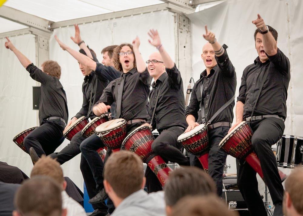 Seven drummers in black onstage at a corporate hospitality event
