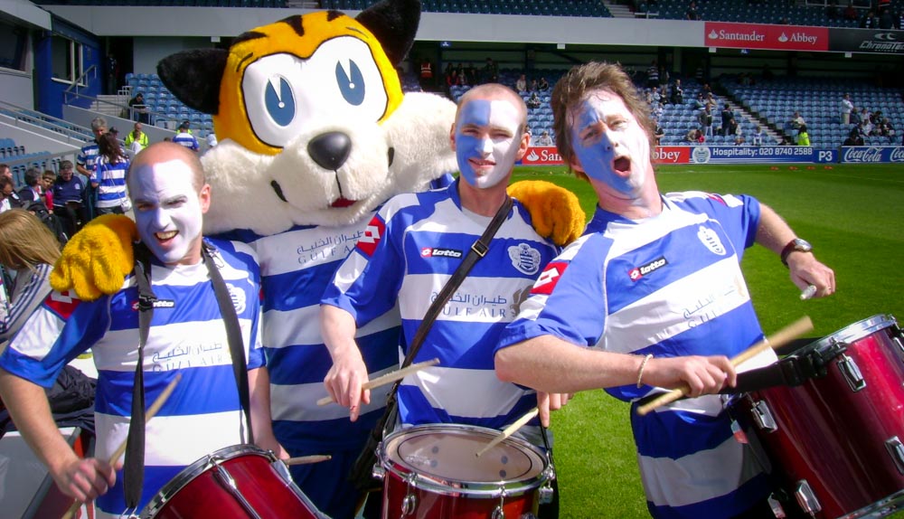 Facepainted drummers on a sports pitch with a mascot - family fun days
