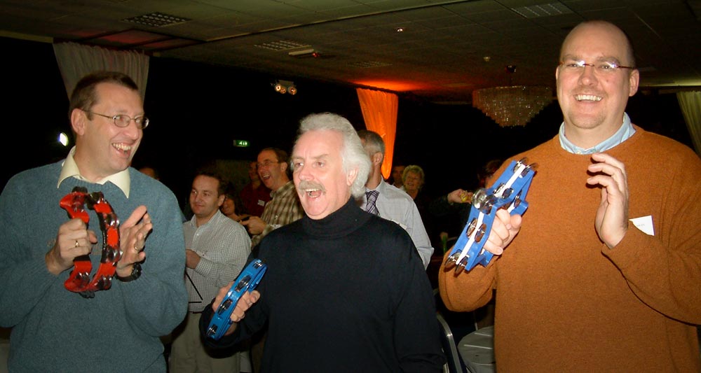 Three men playing tambourines during an evening team-building activity for companies undergoing change